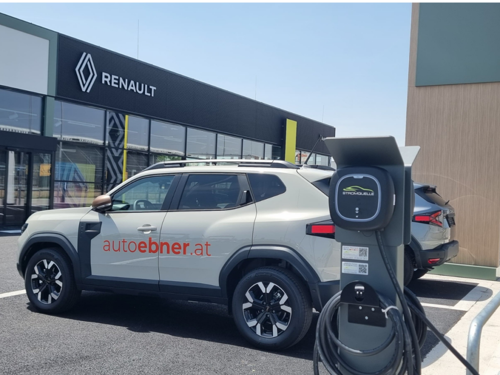 Eine Stromquelle-Ladestation auf dem Parkplatz von Auto Ebner vor dem Renault-Gebäude. Im Vordergrund steht ein Auto mit der Beschriftung 'autoebner.at', während weitere Fahrzeuge im Hintergrund geparkt sind. #Wallbox Pulsar Pro #Eisenstadt