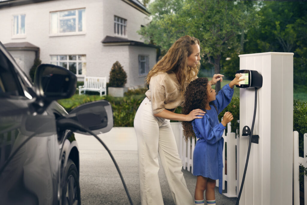 Frau mit Kind die Ihr Auto mit einer Ladestation von Stromquelle aufladen